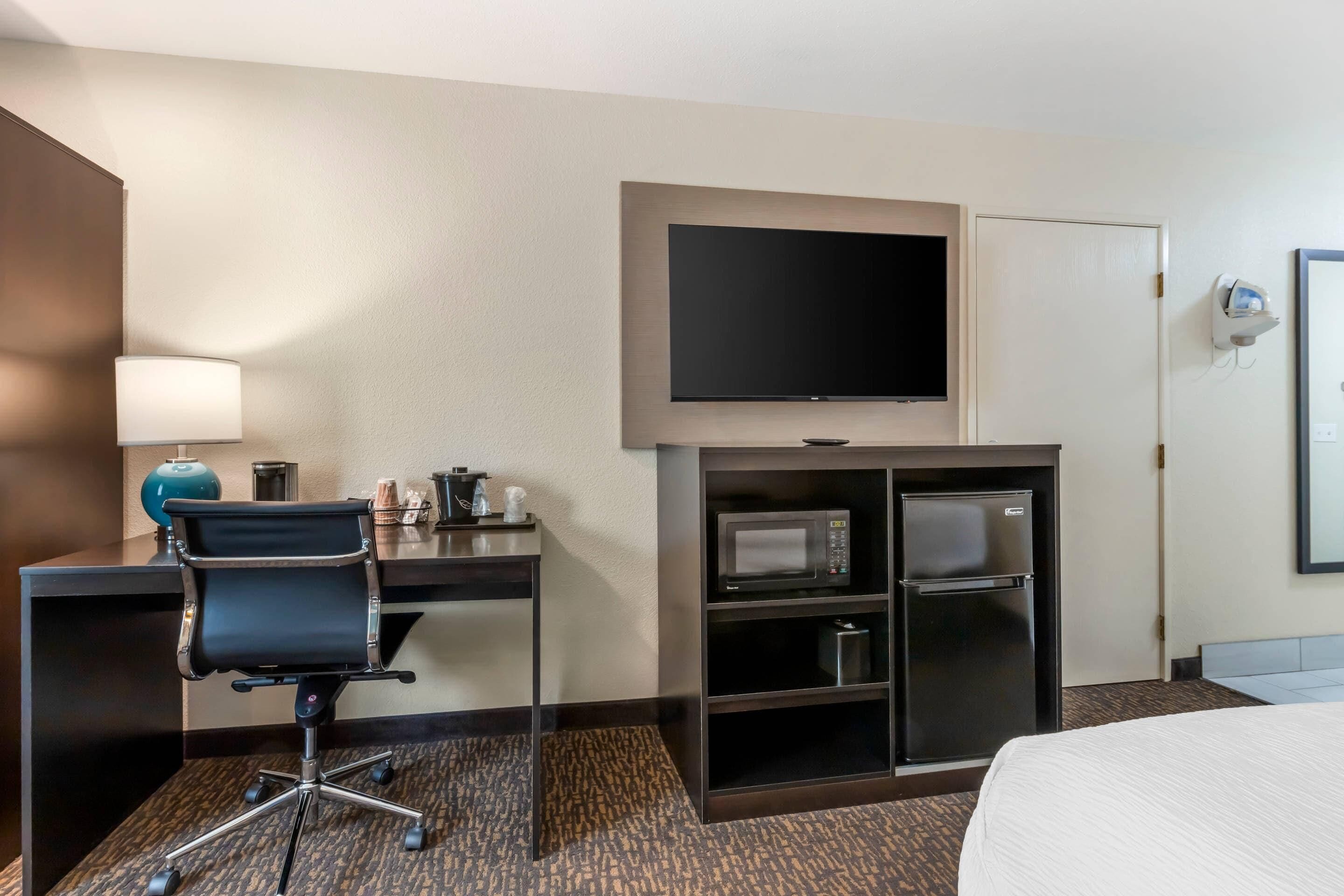 Ein Hotelzimmer mit Schreibtisch, Stuhl, Fernseher, Minibar und einem Bett.