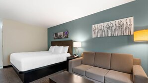 A hotel room with a bed, a sofa, a coffee table, and artwork on the walls.