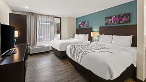Habitación de hotel con dos camas, televisión, escritorio y ventana con cortinas.