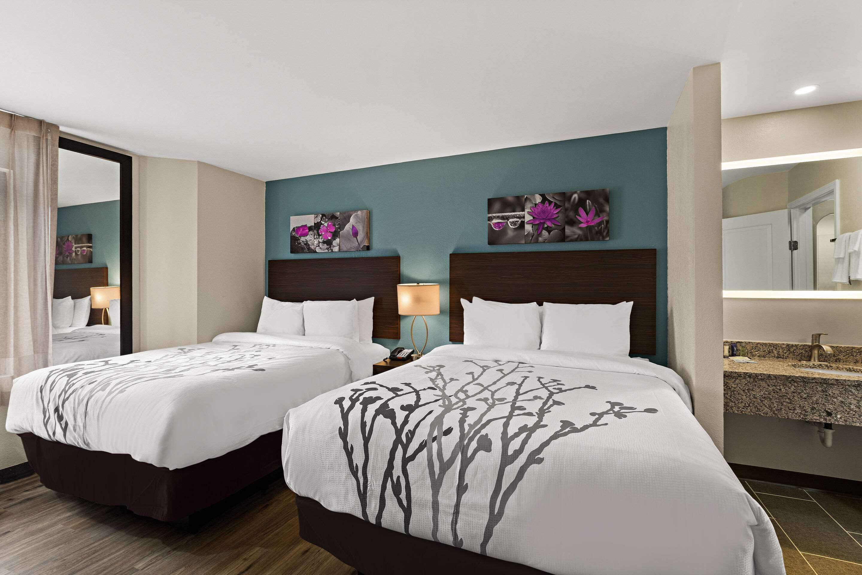 Een hotelkamer met twee bedden, een badkamer met een wastafel en kunstwerken aan de muren.