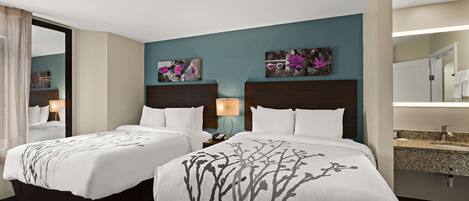 Een hotelkamer met twee bedden, een badkamer met een wastafel en kunstwerken aan de muren.