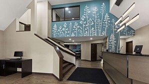Un moderno vestíbulo de hotel con una escalera de madera, un mostrador de recepción y una pared con un mural de un árbol.