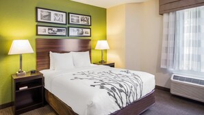 A hotel room with a bed, two bedside tables with lamps, a nightstand, a wall with framed pictures, and a window with curtains.