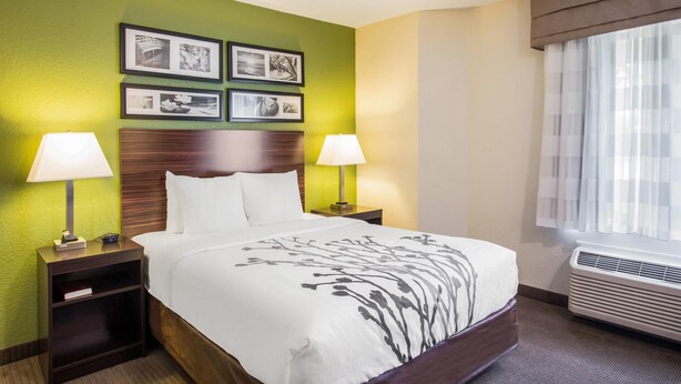 Habitación de hotel con cama, dos mesitas de noche con lámparas, un aparador y una ventana con cortinas. En la pared, varias fotografías enmarcadas.