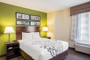A hotel room with a bed, two bedside tables with lamps, a nightstand, a wall with framed pictures, and a window with curtains.