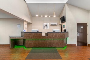 A hotel reception desk with a 'Quality by Choice Hotels' sign, a flat-screen TV, and a digital clock. - Quality Inn Kansas City International Airport (Kansas City)