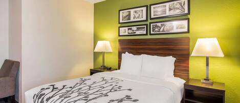 A hotel room with a bed, two bedside tables, a chair, and a wall with framed pictures.