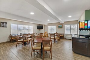 Un vaste espace dédié à la salle à manger, avec des tables et des chaises en bois, un téléviseur à écran plat fixé au mur et des fenêtres ornées de motifs représentant des paysages urbains.