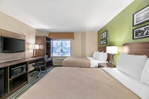 Une chambre d’hôtel comprenant un lit, un bureau avec un téléviseur à écran plat, une chaise, une fenêtre donnant sur un paysage aux formes géométriques et un mur orné de tableaux.