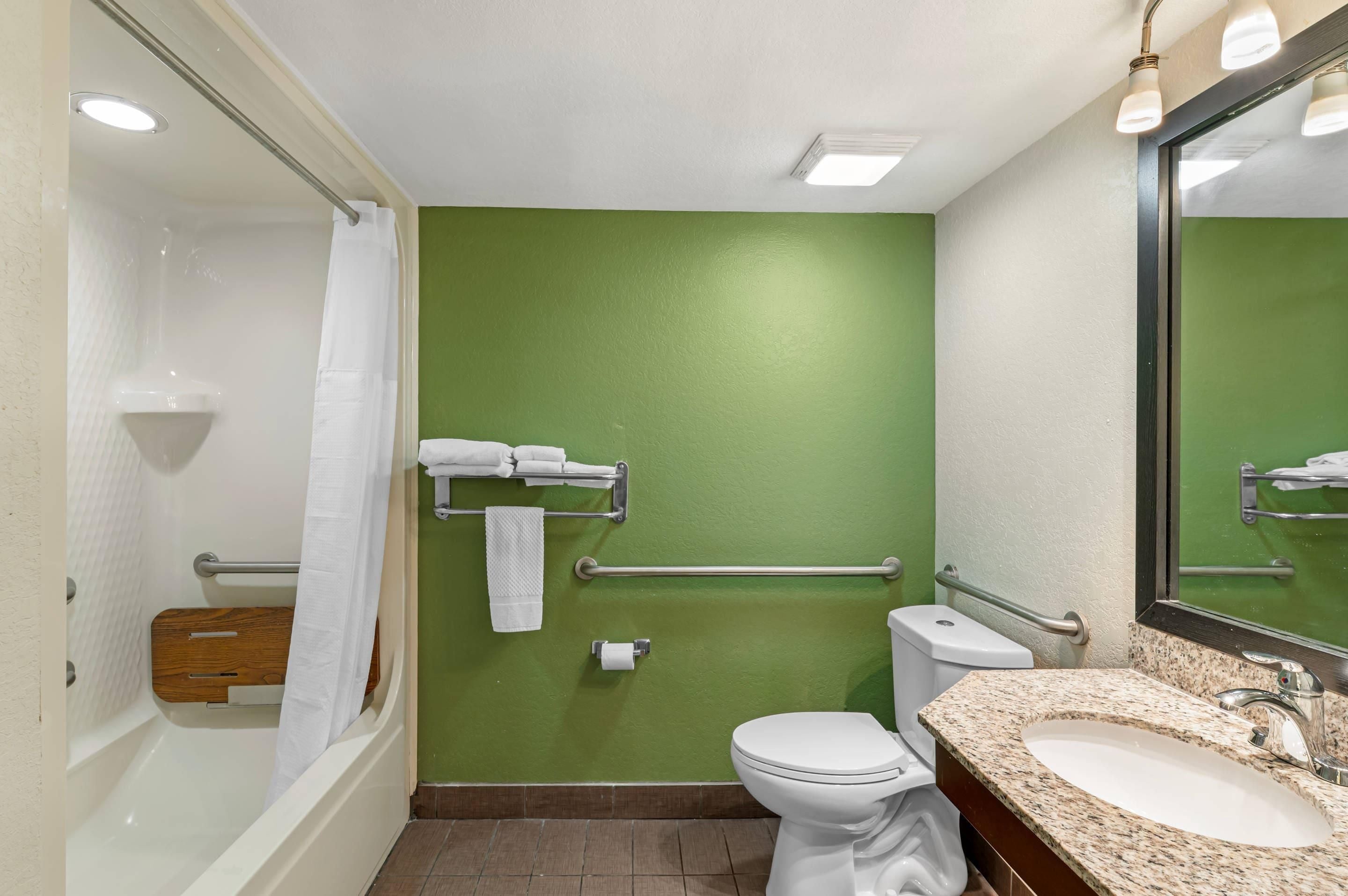 Un baño con pared verde, inodoro blanco, lavamanos con encimera de granito y zona de ducha.