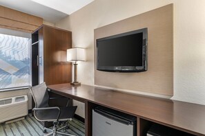 A hotel room with a desk, a chair, a television mounted on the wall, and a window with a view of a building. - Quality Inn Kansas City International Airport (Kansas City)