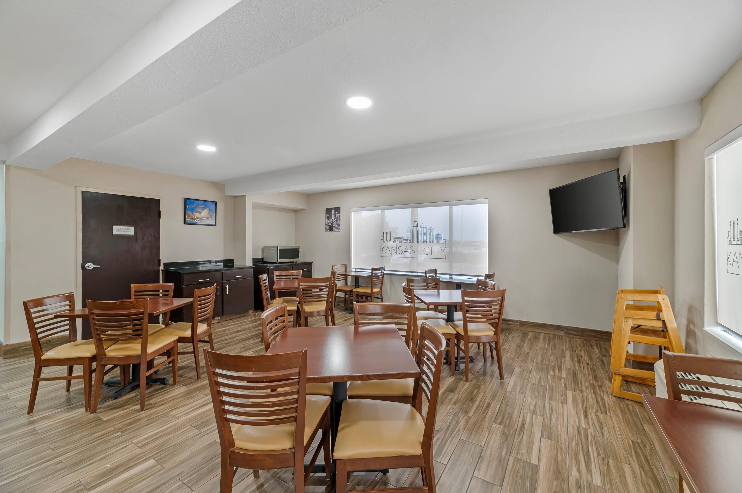 Comedor con mesas y sillas de madera, área de cocina con microondas y vista a la ciudad.