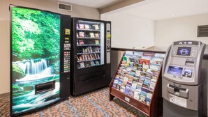 A hotel lobby with a waterfall display, a snack vending machine, a magazine rack, and an ATM.