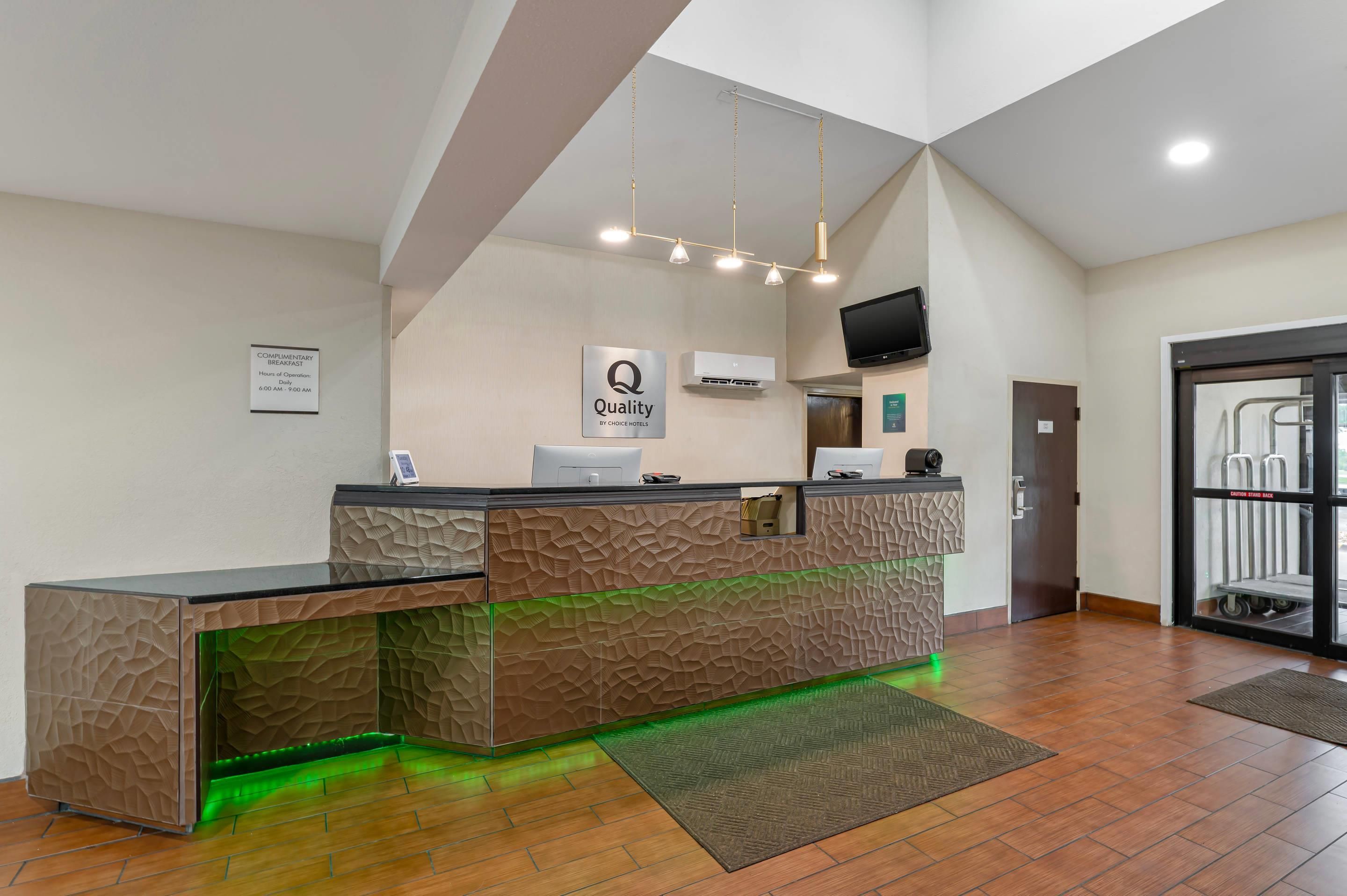 A hotel reception area with a modern design, including a reception desk, a sign for complimentary breakfast, and a television mounted on the wall.