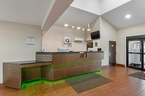 Ein modern gestalteter Hotel-Empfangsbereich mit einer Rezeption, einem Schild für das kostenlose Frühstück und einem an der Wand befestigten Fernseher.