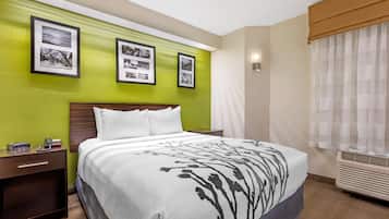 Une chambre d’hôtel avec un lit, une table de chevet, un climatiseur fixé au mur et des tableaux encadrés accrochés au mur.