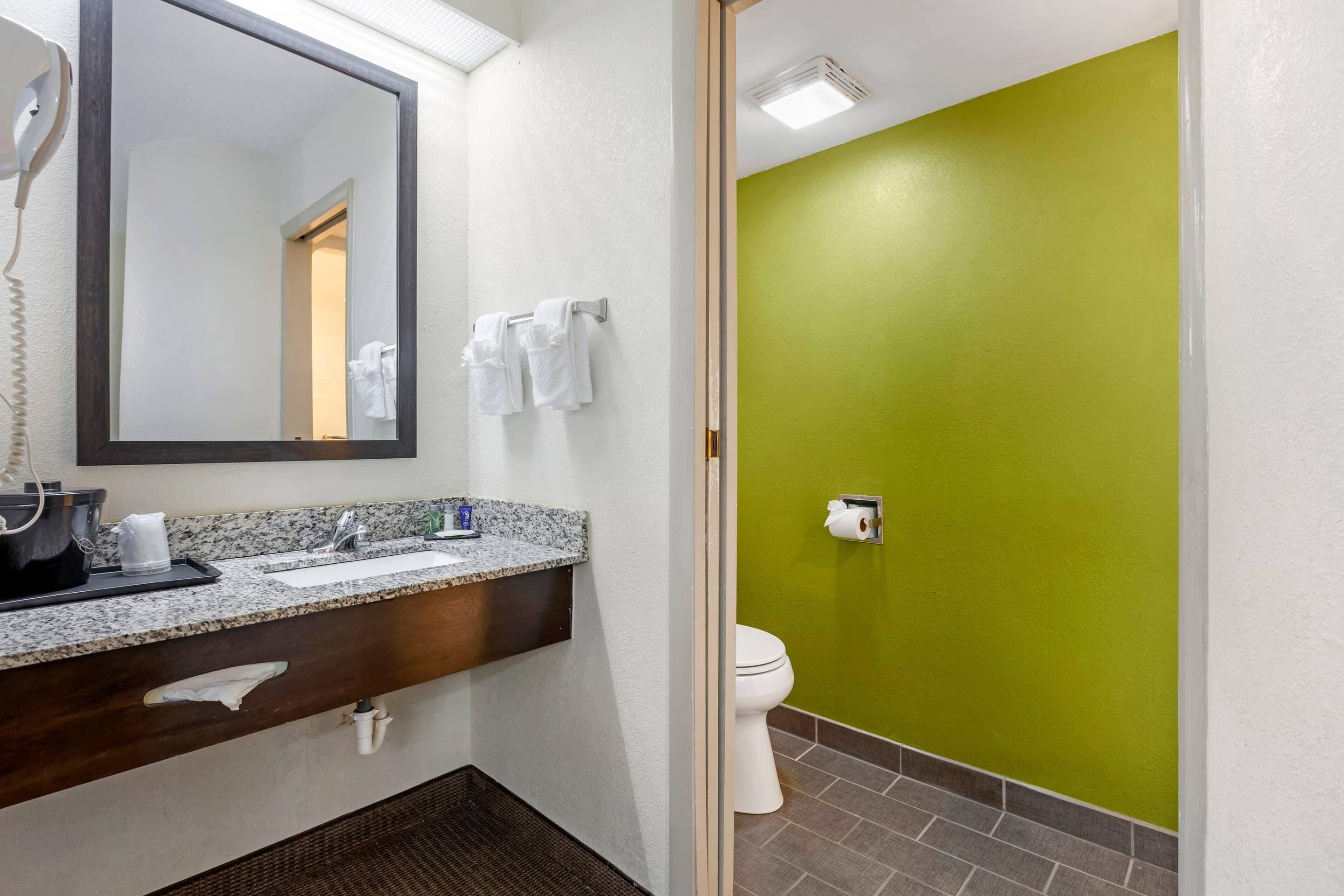 A bathroom with a granite countertop sink, a mirror, a hairdryer, and a toilet.