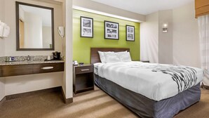 A hotel room with a bed, a nightstand, a mirror, a sink, and framed pictures on the wall. - Sleep Inn at Greenville Convention Cente (Greenville)