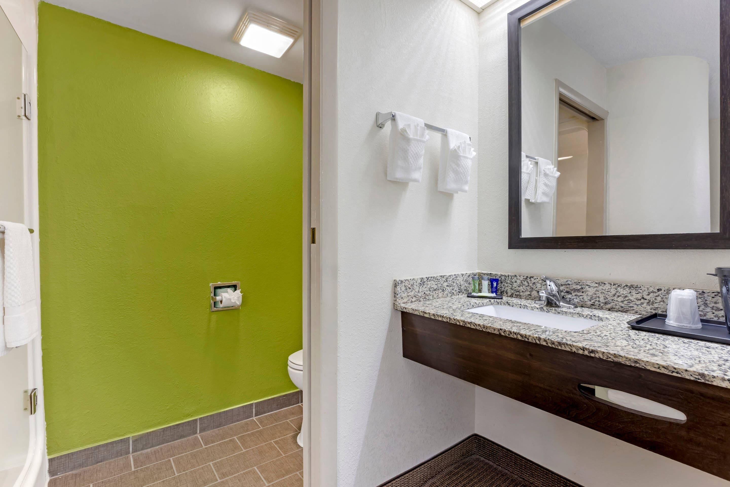 A bathroom with a green wall, a white sink, a mirror, and a towel rack.