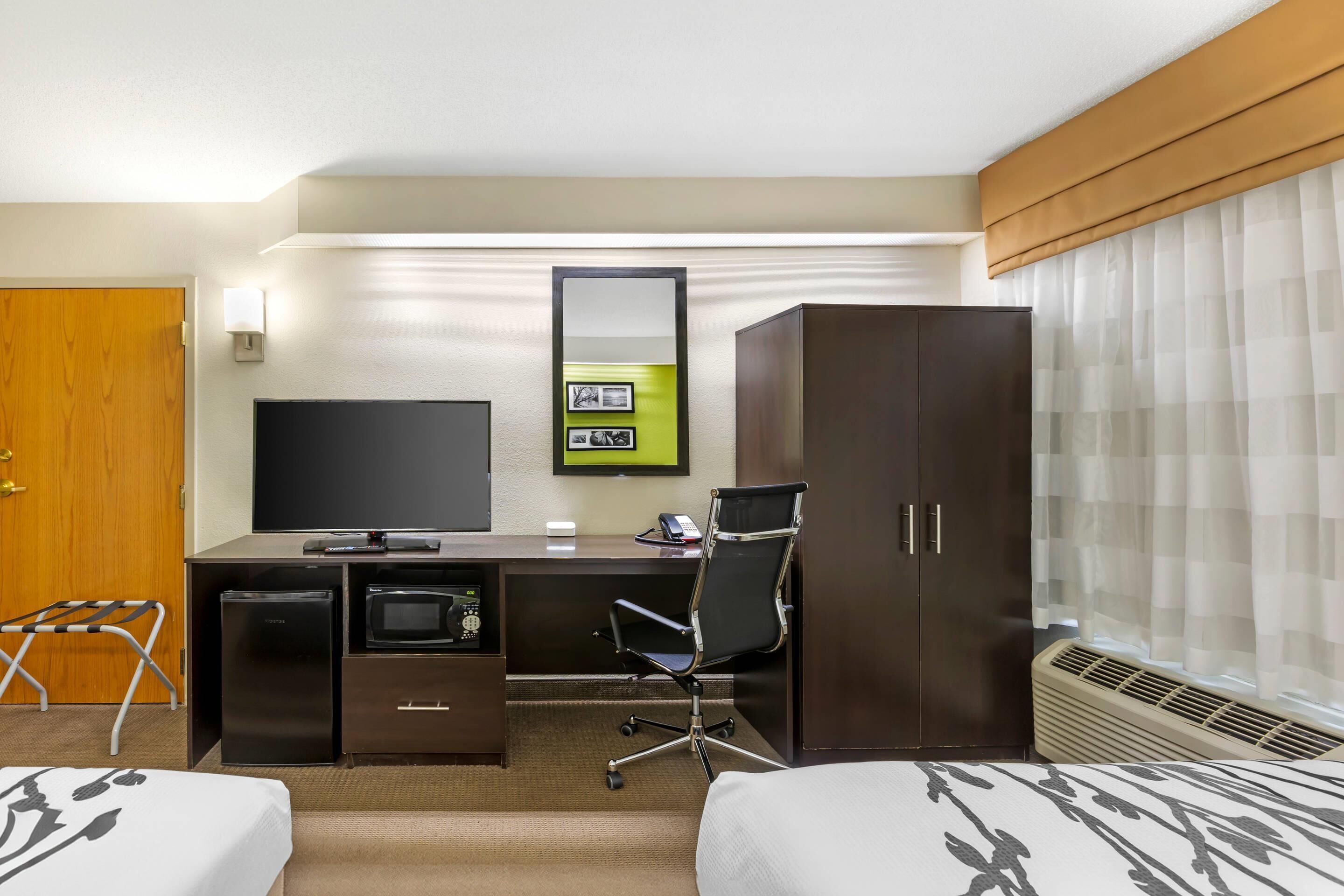 A hotel room with a bed, a desk with a computer, a chair, a TV, and a wardrobe.