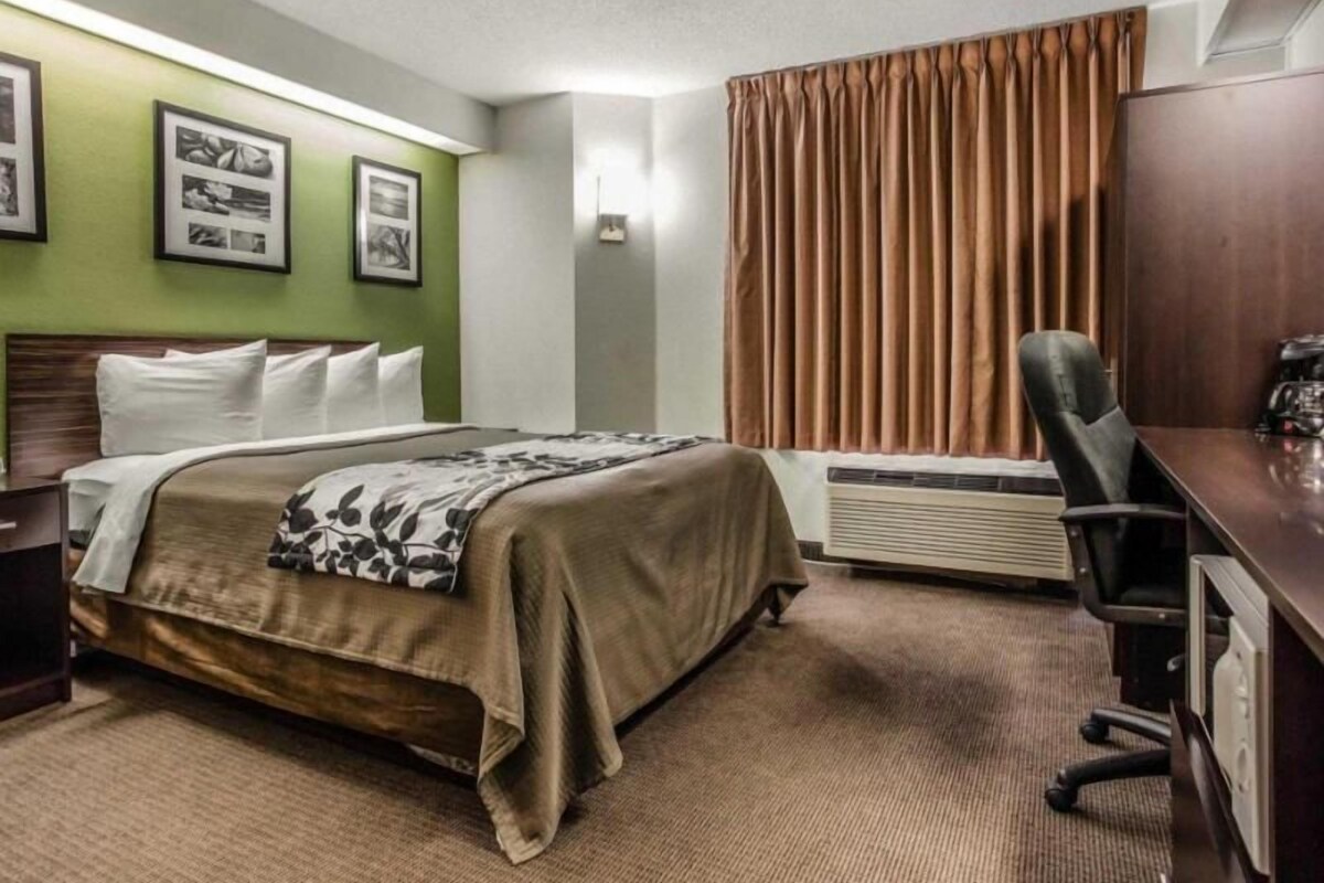 A hotel room with a bed, a desk, a chair, a window with curtains, and framed pictures on the wall.
