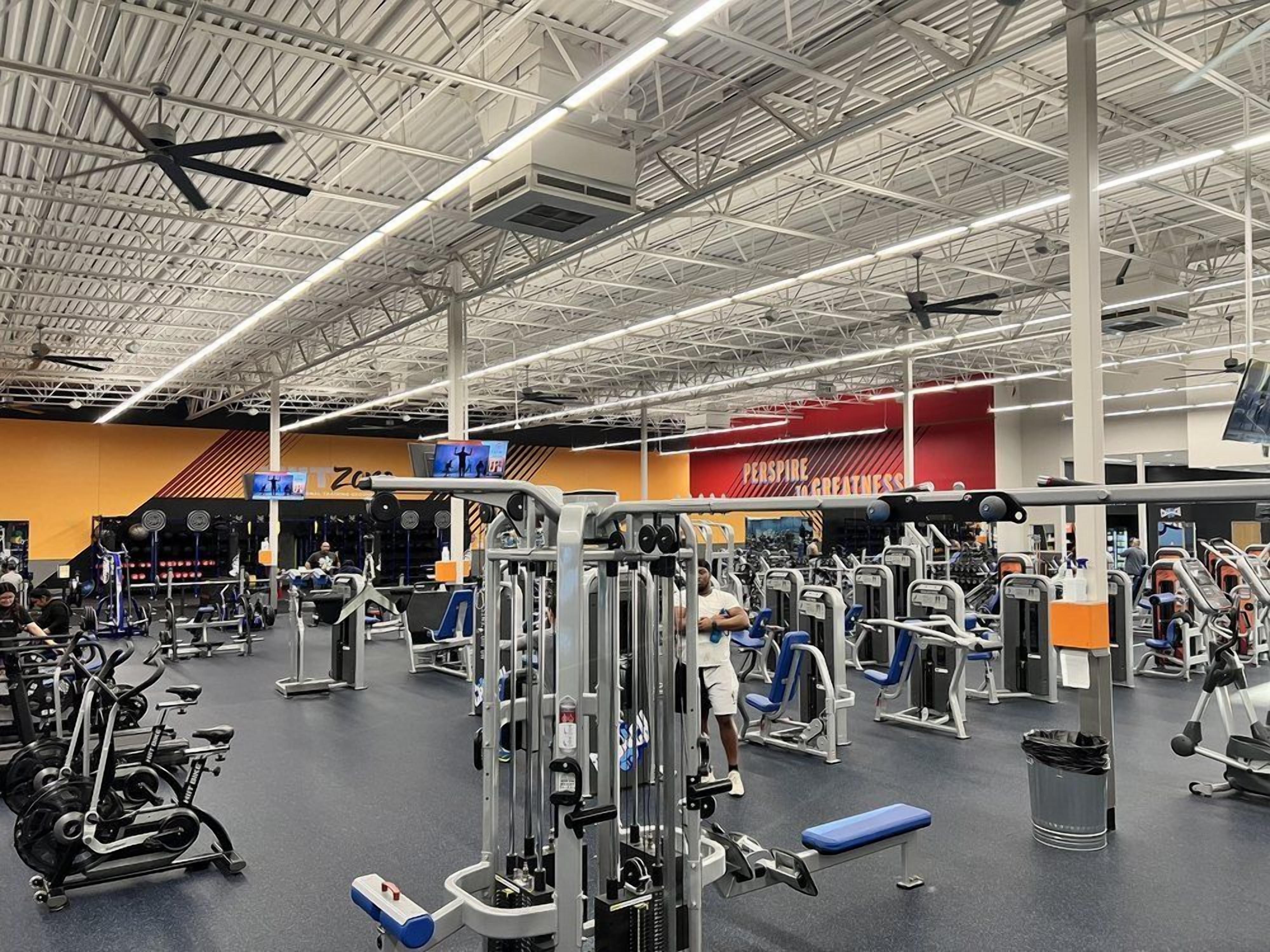 A gym with various exercise equipment, a high ceiling, and a visible brand name 'PERSPIRATE' on the wall.