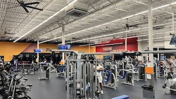 Un gimnasio con diversos equipos de ejercicio, un techo alto y el nombre de la marca 'PERSPIRATE' visible en la pared.