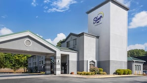 A hotel with a prominent tower featuring the 'Sleep Inn' logo, a covered entrance, and a parking lot. - Sleep Inn at Greenville Convention Cente (Greenville)