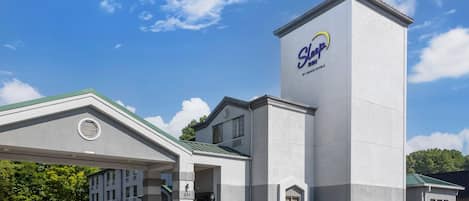A hotel with a prominent tower featuring the 'Sleep Inn' logo, a covered entrance, and a parking lot.