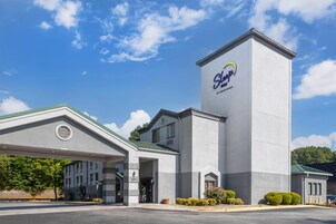 Un hotel con una torre destacada que muestra el logotipo de 'Sleep Inn', una entrada cubierta y un estacionamiento.