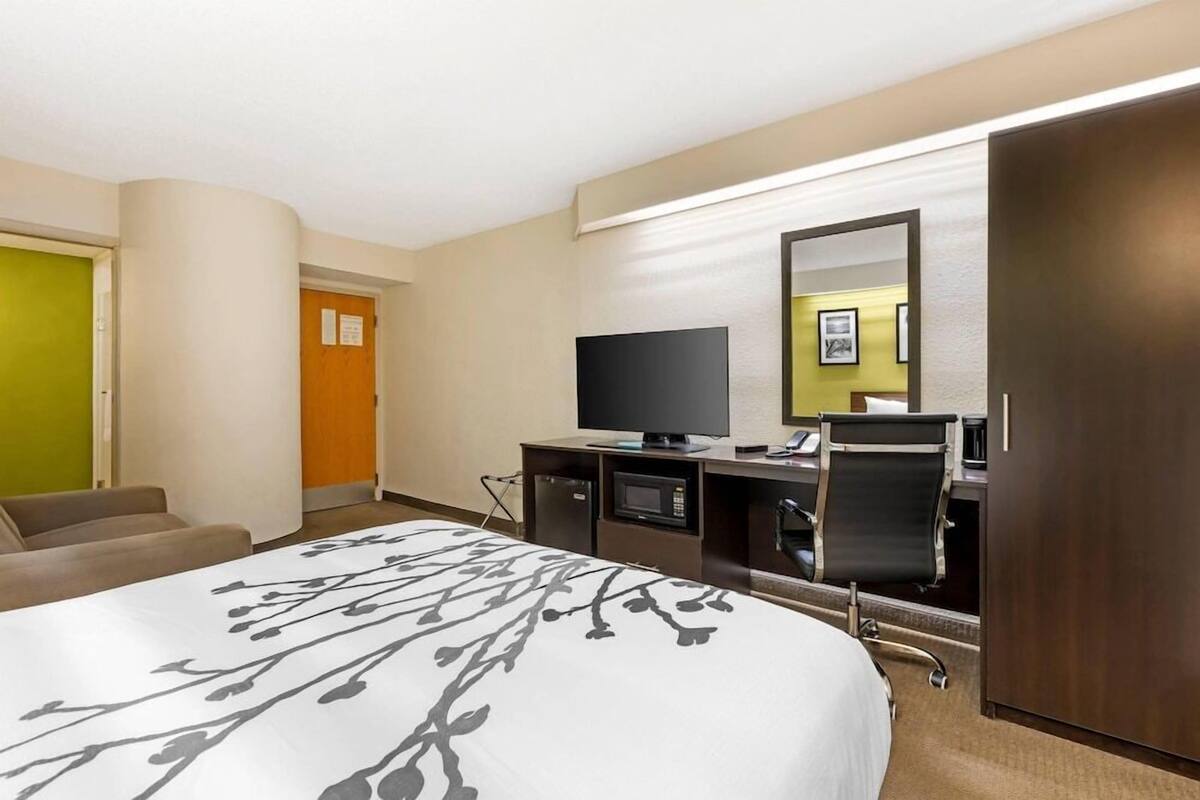 A hotel room with a bed, a TV, a desk with a computer, a microwave, and a seating area.