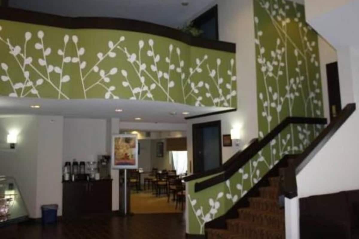 A hotel lobby with a staircase, a reception desk, and a dining area in the background.