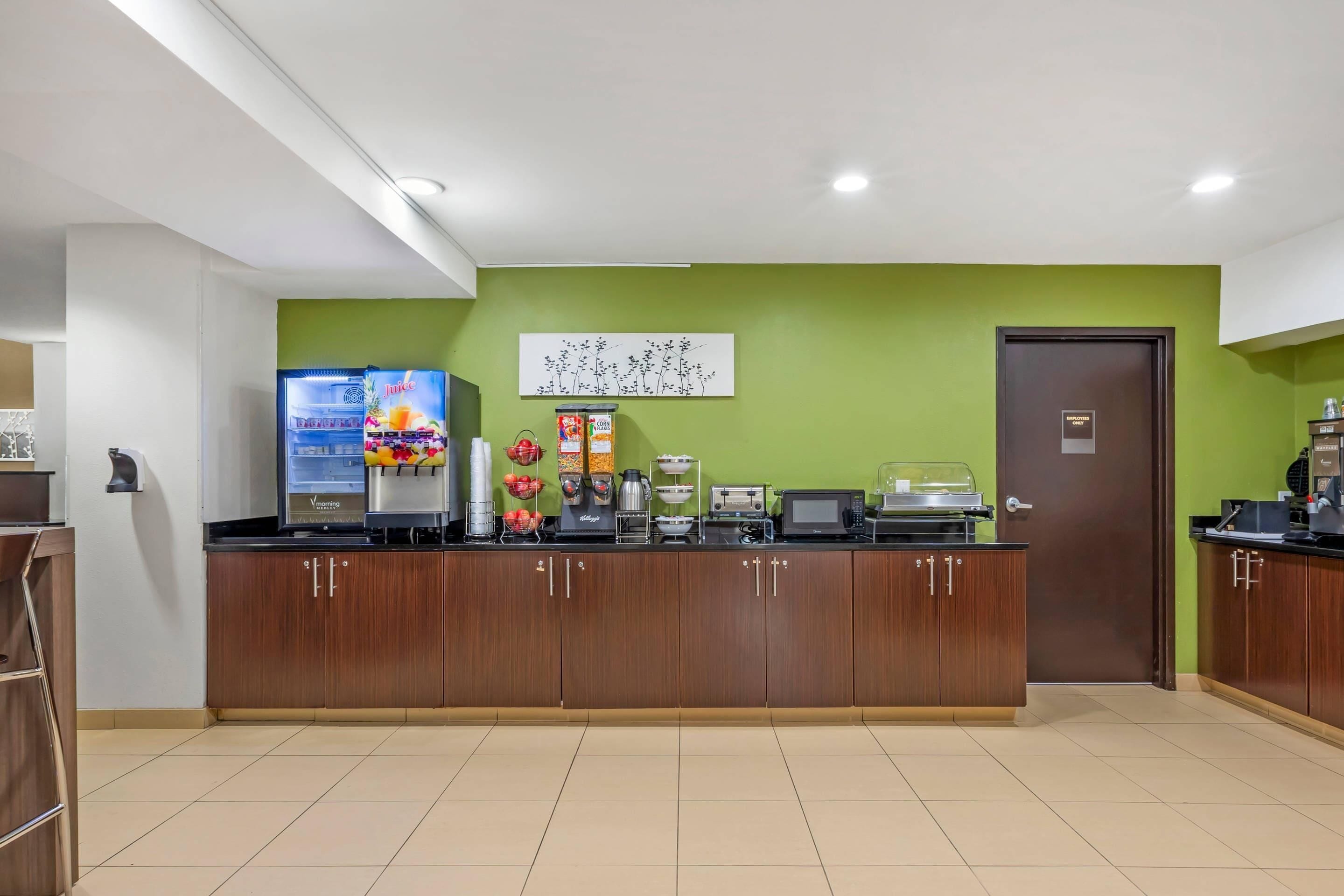 Un espace cuisine propre et moderne, équipé d’un distributeur de jus, d’un four à micro-ondes et de divers produits alimentaires disposés sur le comptoir.