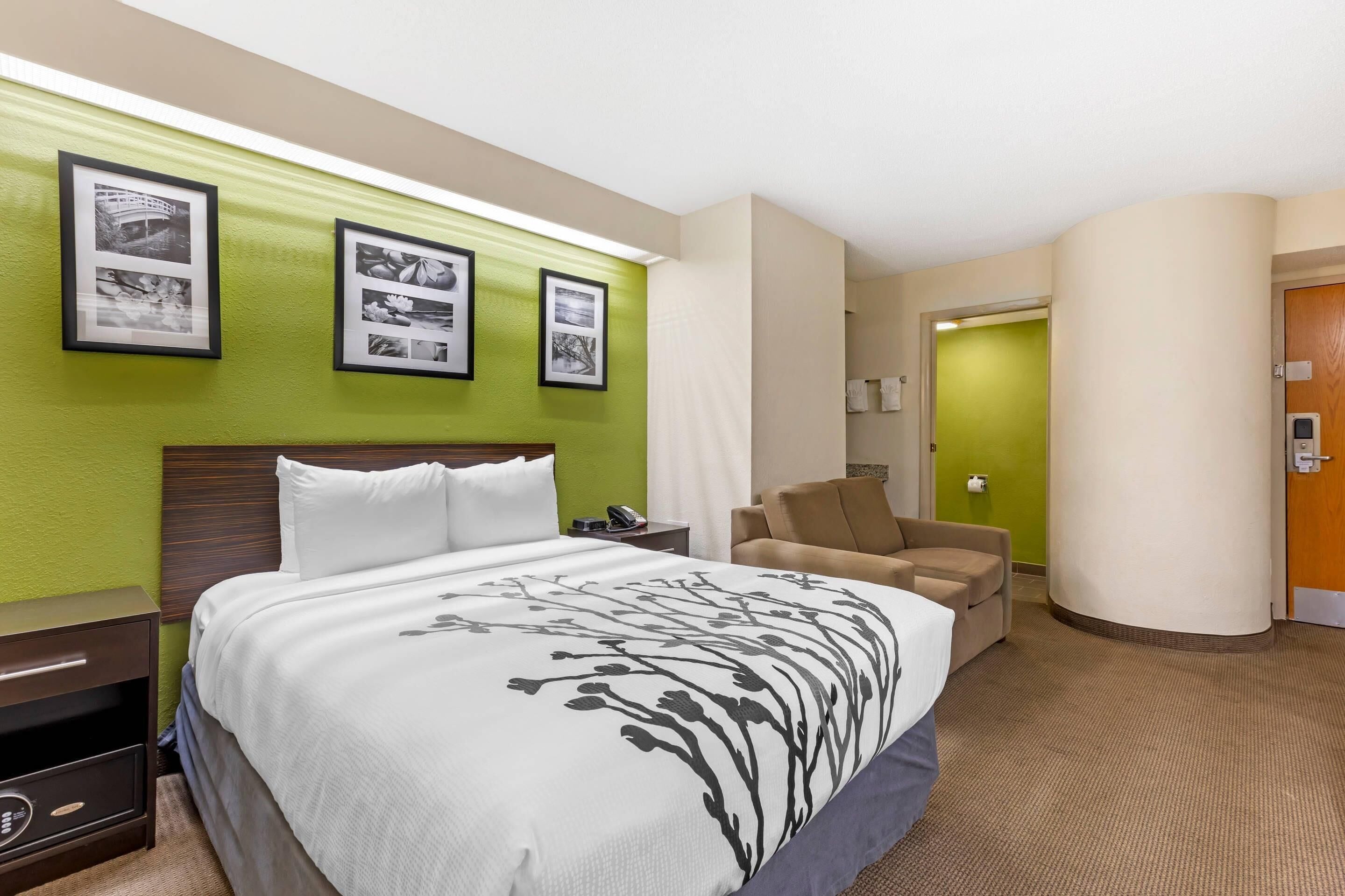 A hotel room with a large bed, a chair, a nightstand, and framed pictures on the wall.