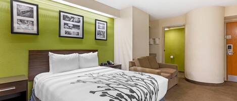 A hotel room with a large bed, a chair, a nightstand, and framed pictures on the wall.