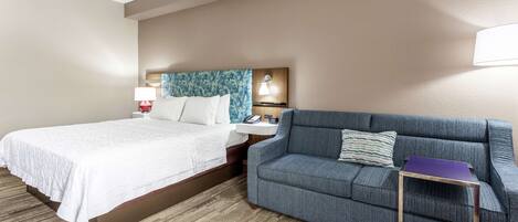 A hotel room with a bed, a blue sofa, a small table, and a nightstand with a lamp.