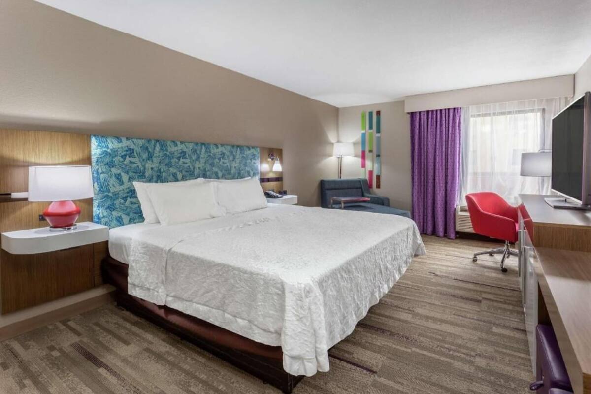 Une chambre d’hôtel avec un grand lit, un bureau, une chaise, une télévision et une lampe.
