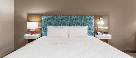 Habitación de hotel con una cama grande, dos mesitas de noche, una lámpara roja, una lámpara blanca y un cabecero azul con estampado.
