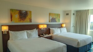 A hotel room with two beds, bedside lamps, and artwork on the wall.