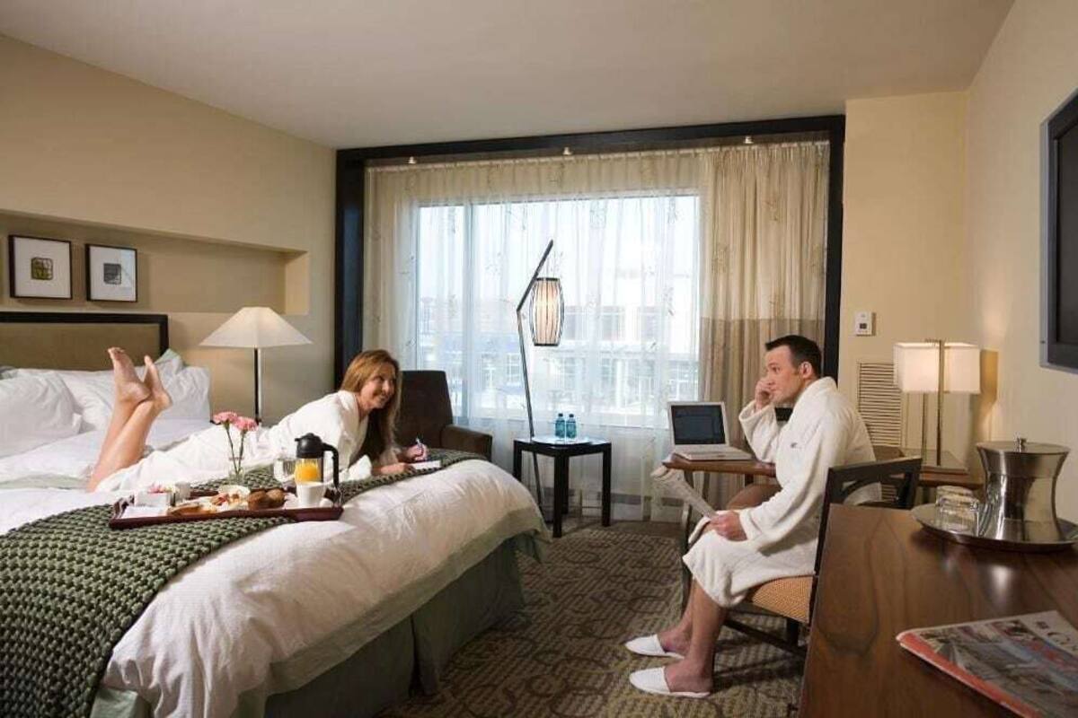 A hotel room with a bed, a desk, a chair, a laptop, and a window with curtains.