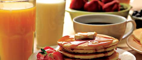 Un desayuno con tortitas, fresas y un vaso de zumo de naranja.
