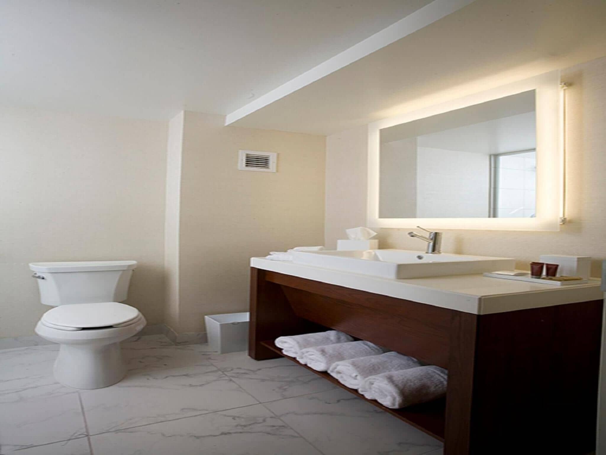 Une salle de bain moderne équipée de toilettes, d’un lavabo avec miroir et d’un porte-serviettes.