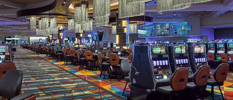 A casino with rows of gaming machines and chairs, a colorful carpet, and hanging chandeliers.