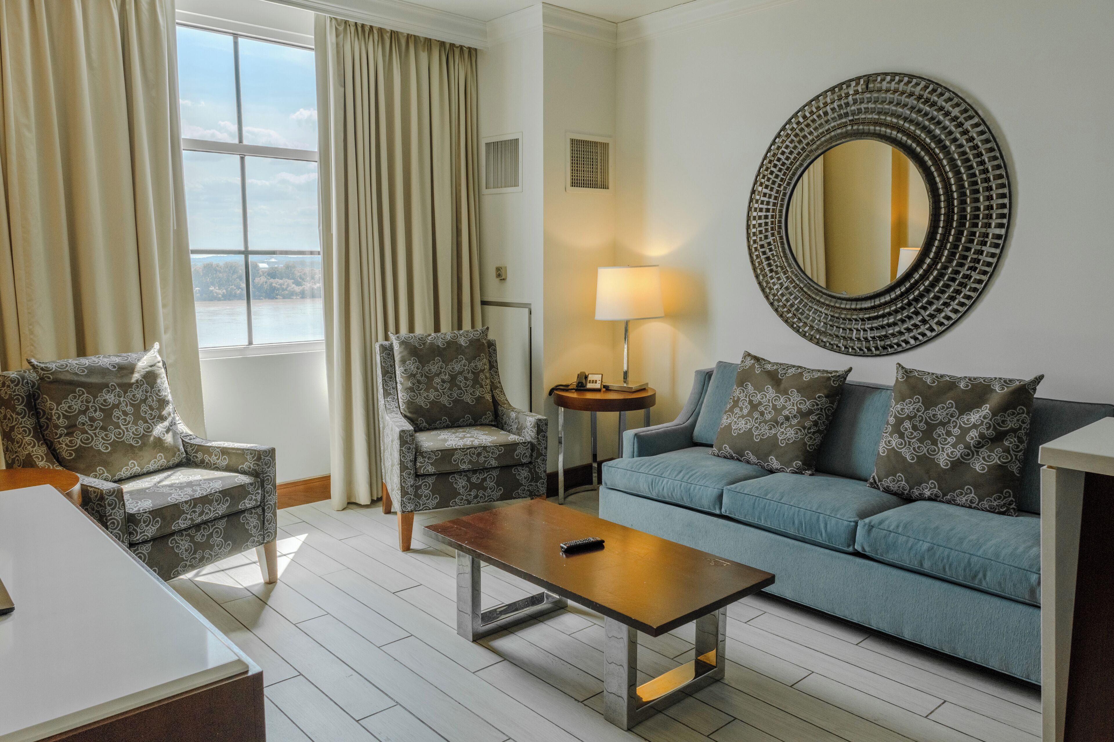 A living room with a sofa, armchair, coffee table, and a round mirror on the wall.