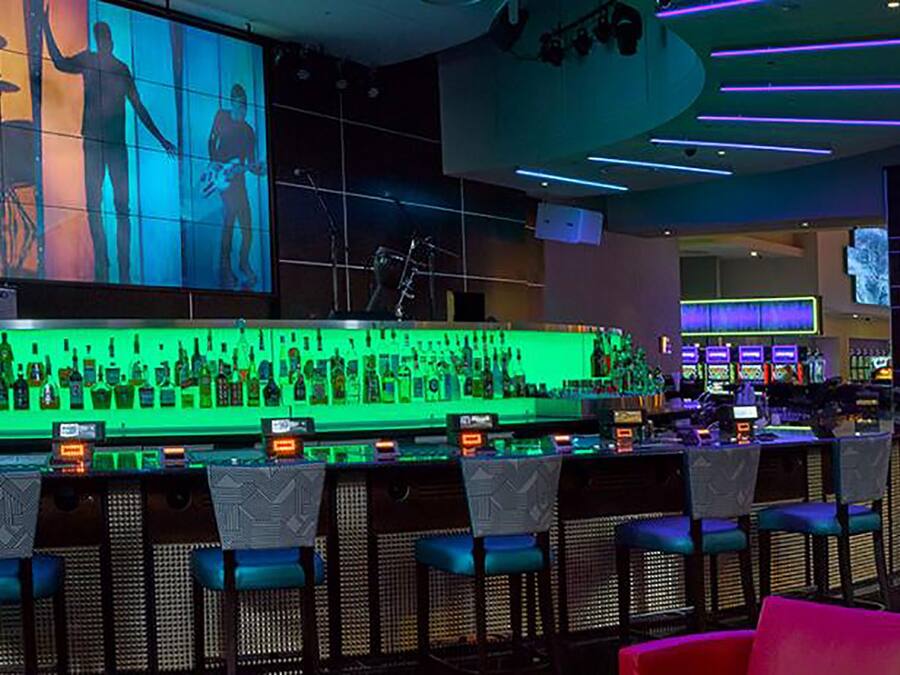 A bar area with a green-lit bar counter, multiple seating options, and a large screen displaying silhouettes of people.