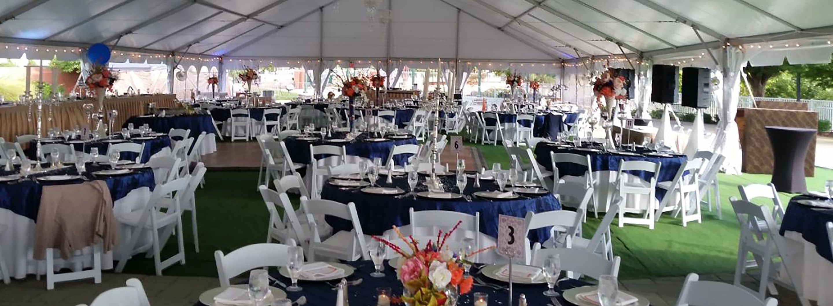 Un espace événementiel aménagé sous une tente, avec des tables dressées pour un événement formel, des chaises blanches et des décorations florales.