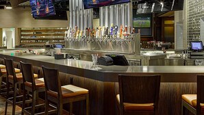 A bar area with multiple seating options, a long counter with a variety of taps, and multiple screens displaying sports events.