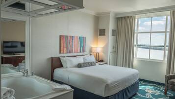 Une chambre d’hôtel avec un grand lit, une salle de bain avec un lavabo et un miroir, une télévision et une fenêtre avec des rideaux.