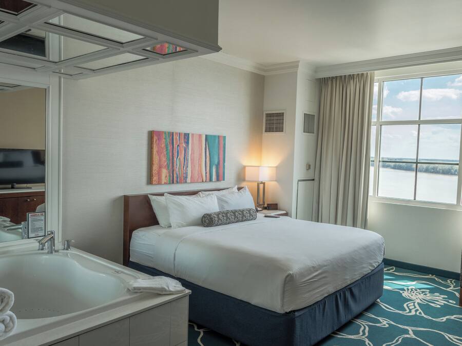 Une chambre d’hôtel avec un grand lit, une salle de bain avec un lavabo et un miroir, une télévision et une fenêtre avec des rideaux.