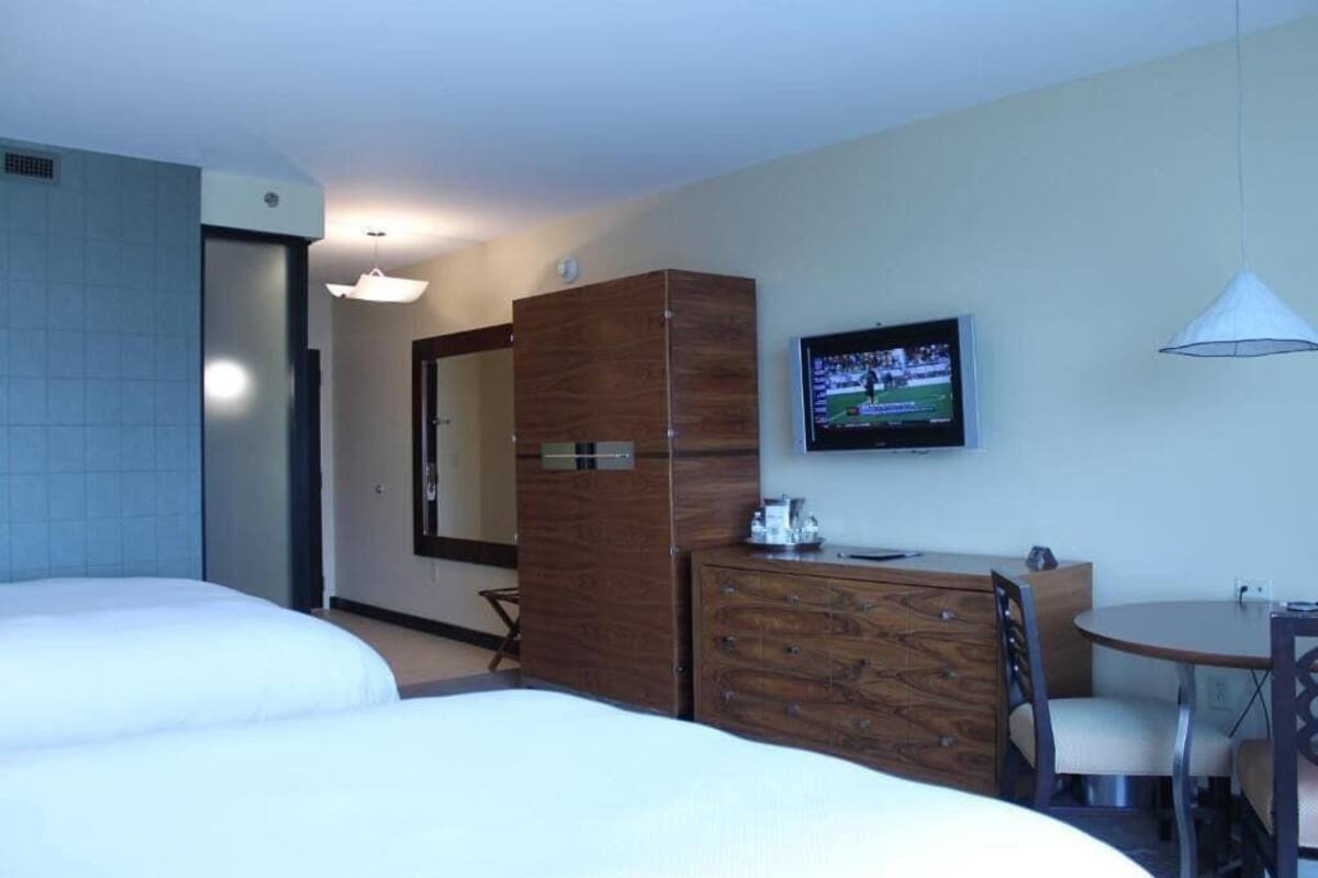 A hotel room with two beds, a wooden dresser, a television, and a small table with chairs.